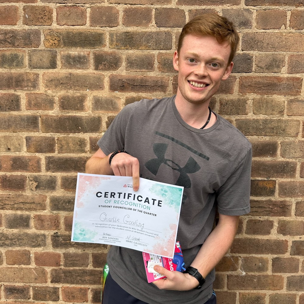 Person with short ginger hair wearing a grey tshirt holding up a certificate 
