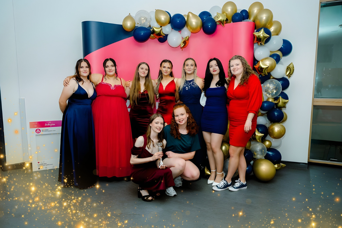 A group of students standing in front of a balloon arch and a promotional banner at a student event.